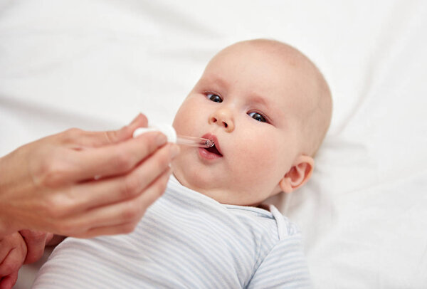 Mother giving liquid vitamins to child.