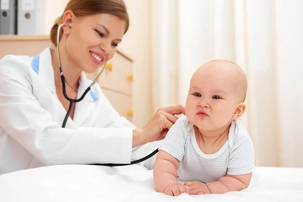 Little baby visiting doctor. Young cheerful female nurse listening child with stethoscope in clinic.