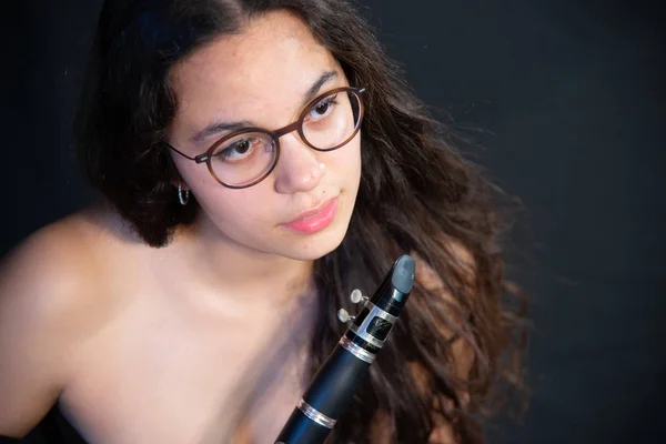 A brunette girl with her clarinet, with glasses, with bare shoulder, on a black uniform background