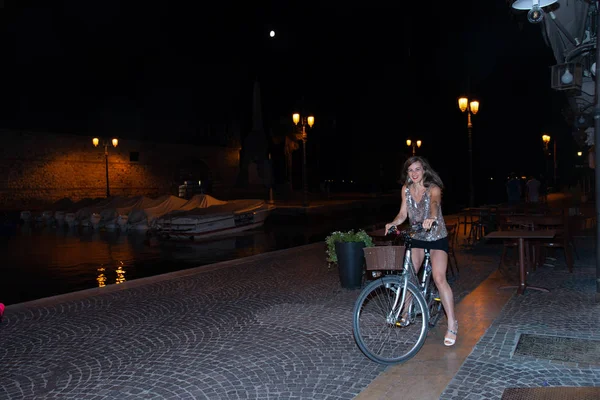 night scene with a girl on a bike at the port of Lazise, Lake Garda, Italy