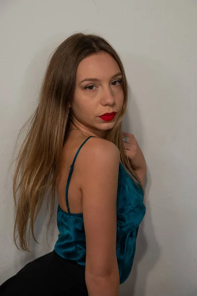 Half-length portrait of blonde girl in blue satin tank top with lace. Perfect makeup with red lips. White background. Copy space.