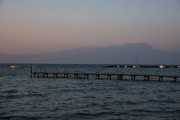 Wooden pier and concrete pier for mooring boats on the lake. Beautiful winter sunny day with grazing light. Some boats are docked at the dock. A sailboat in the middle of the lake. Background with mountains