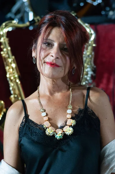 Close-up of a serious lady posing while she is wearing a petticoat dress with lace inserts, combined with a pink viscose stole. Perfect makeup, necklace around the neck, red hair. Musical instruments background.