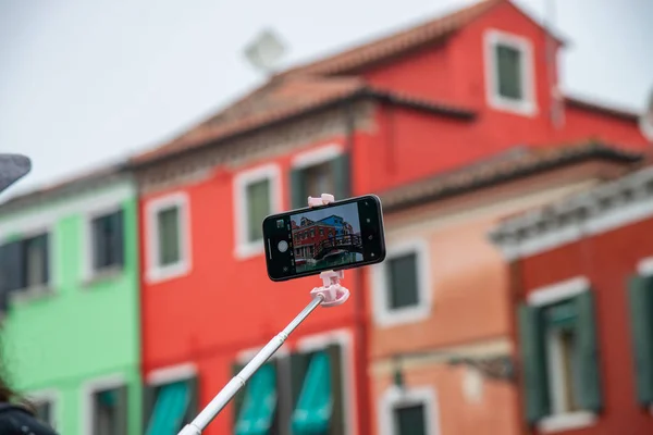 Colorful houses in Burano island near Venice, Italy. In photography, detail of a mobile phone while photographing the colorful houses and a wooden bridge.