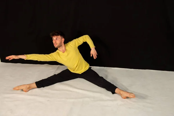 Male dancer with black trousers and yellow t-shirt, practicing in the studio on a black background. The attractive young man shows modern dance poses.