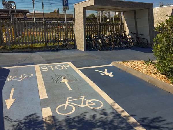 A bike path and a pedestrian street, and bicycle racks in a pedestrian area with many bicycles parked. Horizontal and vertical signs for cycle and pedestrian paths.