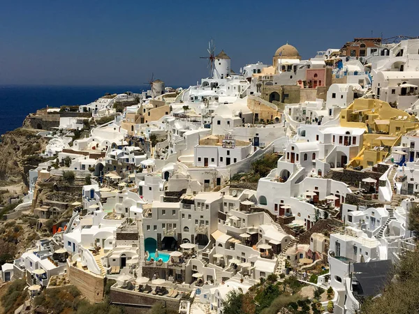 Panorama with characteristic white houses of Oia in Santorini volcanic island of the Aegean Sea in Greece. Gulf of the caldera with hotels with swimming pools, mills turned into restaurants and Greek churches.