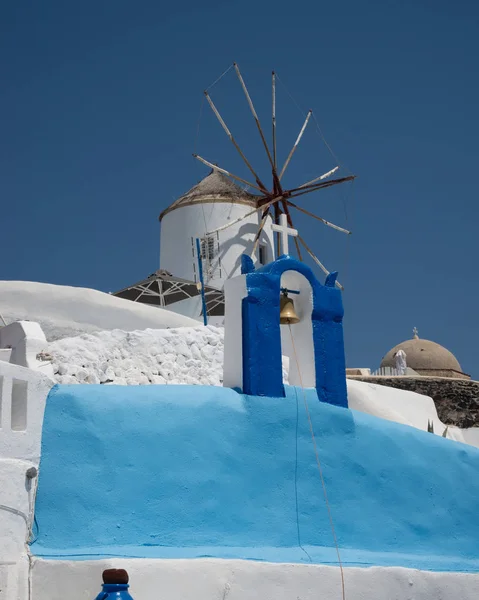 White houses and blue roofs characteristic of housing in Santorini island in Greece. Typical urban agglomeration with houses, church with bell tower with bells and national flag.