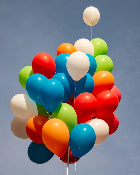 Group of multi colored balloons tied together in the blue sky. Country of Cento, Italy, during the Carnival event to be presented to the public.