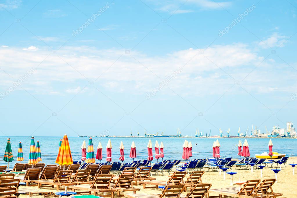 Aerial view to sandy beach of Adriatic sea in Albania, full of umbrellas and sunbeds, Port of Durres in horizon
