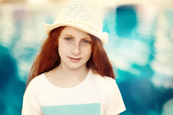 Close-up facial portrait of beautiful little child girl with red hair and freckles standing in front of the pool — Stock Photo, Image