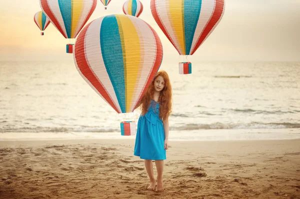 Retrato conceptual de niña pequeña con el pelo rojo y pecas de pie en una playa con globo de aire caliente colorido — Foto de Stock