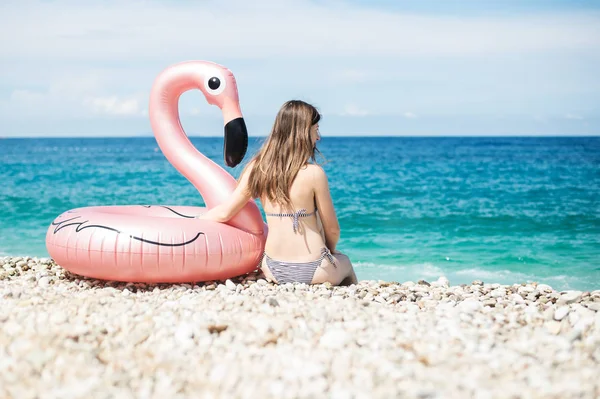 Młoda kobieta z bikini siedzi blisko olbrzymie zawyżone flamingo na plaży z turquois wody Morza Jońskiego Albanii — Zdjęcie stockowe