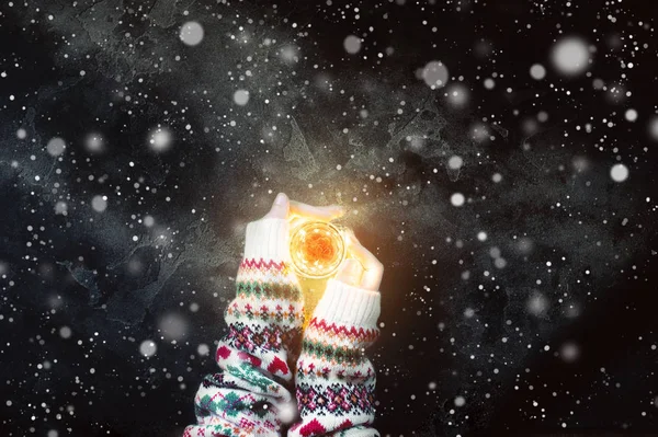 Woman hands in warm sweater holding a candle with bright light. Top view point.