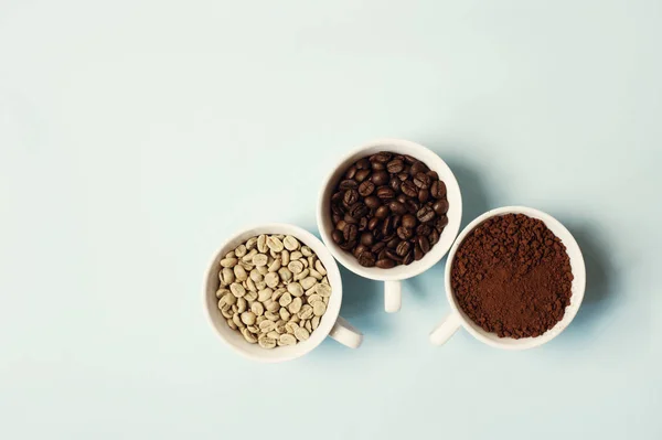 Different types of coffee - ground, grain and unroasted on blue pastel background