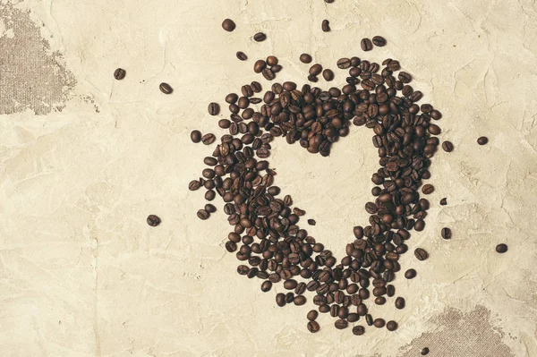 Biji kopi dalam bentuk hati pada kain latar belakang jute — Stok Foto
