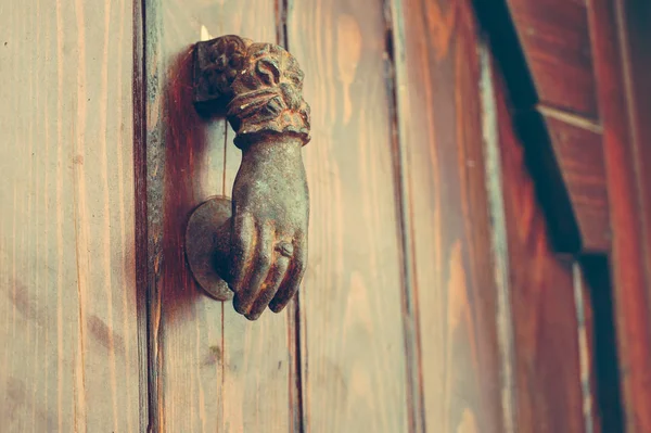 Old wooden door with a brass metal sounder in the form of a small hand to knock on the door.