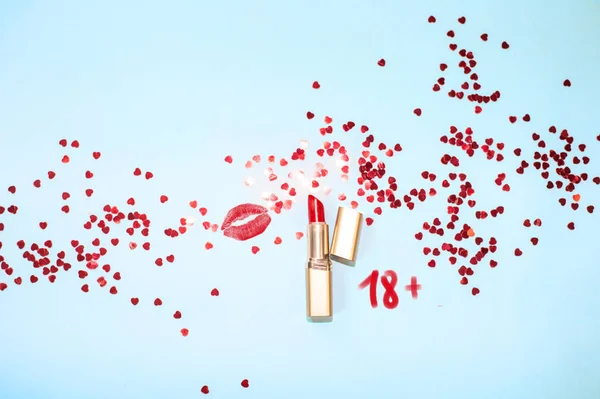 Top view red lipstick kiss on blue background with hearts confetti