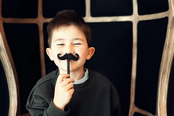 Niño feliz posando con un bigote falso sobre fondo negro — Foto de Stock