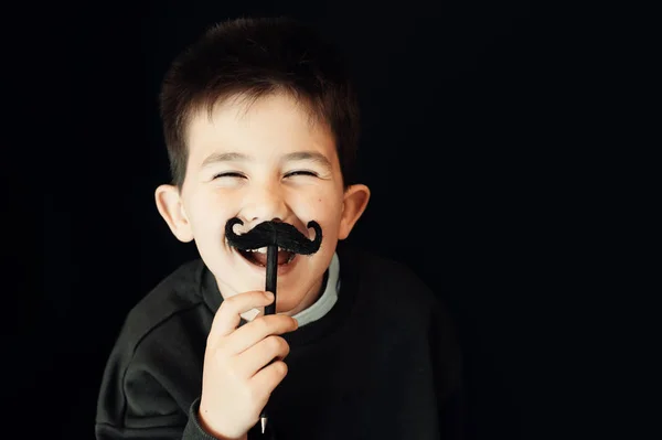 Ragazzo felice in posa con i baffi finti su sfondo nero — Foto Stock