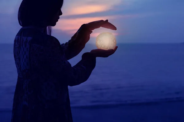 Piękna atrakcyjna dziewczyna na nocnej plaży z piaskiem i gwiazdami trzyma Księżyc w dłoniach — Zdjęcie stockowe