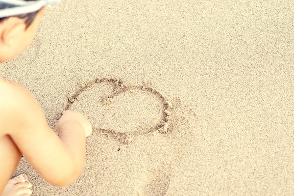 Bambino disegnare il cuore sulla sabbia — Foto Stock