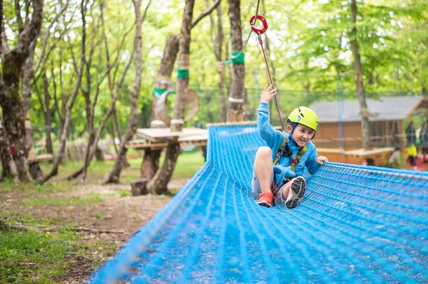 Młody chłopiec przechodzący trasę kablową wśród drzew, sporty ekstremalne w parku przygody — Zdjęcie stockowe