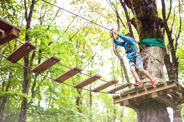 Ung pojke passerar kabel rutt bland träd, extrem sport i äventyrspark — Stockfoto