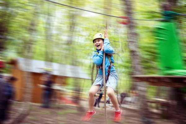 Мальчик, проходящий по канатной дороге среди деревьев, экстремальный спорт в парке приключений — стоковое фото