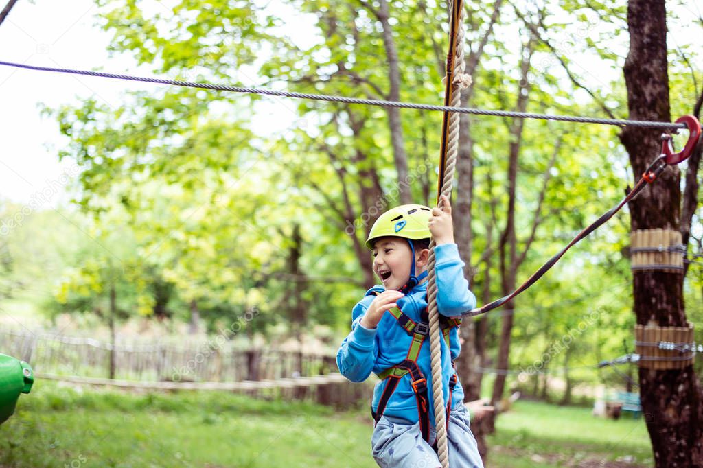 young boy passing cable route among trees, extreme sport in adventure park