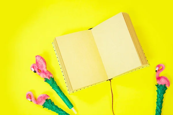 Desktop flatlay: pen with flamingo and pink paper lying vibrant yellow background — Stock Photo, Image