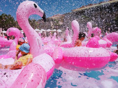 Yetişkinler ve çocuklar yüzme havuzunda şişme flamingolar üzerinde eğleniyor