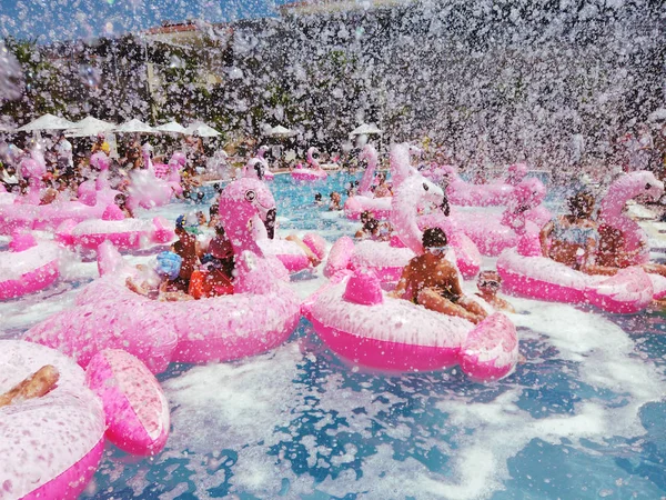 Взрослые и дети веселятся на надувных фламинго в бассейне — стоковое фото