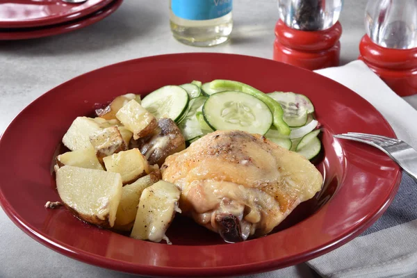 Plate of baked chicken dinner with cheese potatoes and a cucumber salad.