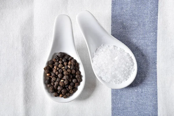 Overhead view of spoons of black peppercorn and rock salt