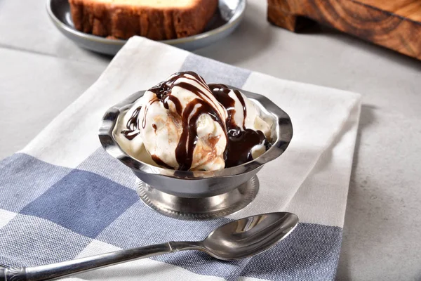A dish of butter pecan ice cream with chocolate syrup.