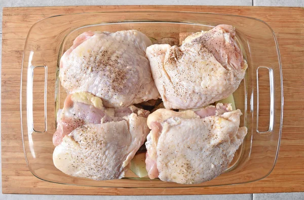 Overhead view of raw chicken thighs on top of diced potatoes in a baking dish