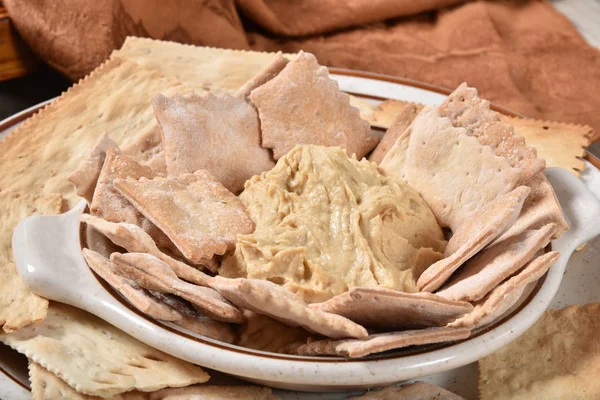 A bowl of hummus with gourmet pita chips and artisan crackers
