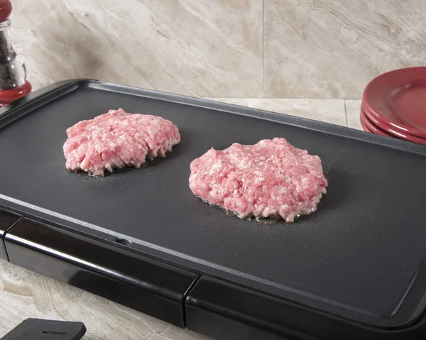 Ground sausage patties cooking on an electric grill.