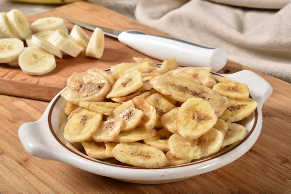 A bowl of dried banana chips with fresh banana