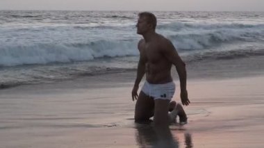 Yakışıklı erkek vücut geliştirmeci sahilde kum diz çökmüş