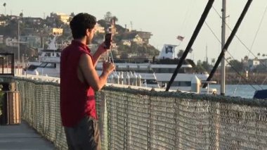 Yakışıklı genç adam akıllı telefon çekim bir Marina ve sosyal medya için deftere nakil