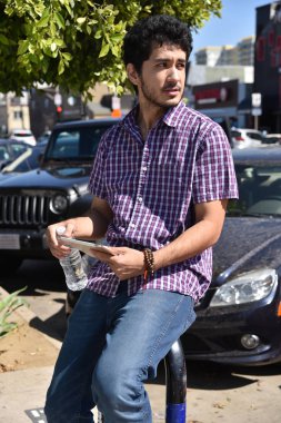 Yakışıklı bir genç adam sokakta küçük sahil kasabası yakınındaki bir tablet bilgisayar ile oturan.