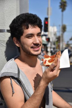 Mutlu bir genç adam bir dilim biberli pizza yeme bir sokak lambası karşı yaslanmış