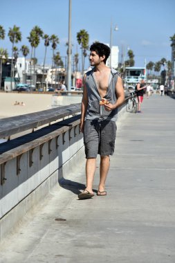 Mutlu bir çok etnik gruptan oluşan genç adam iskelede yürürken bir dilim pizza yeme