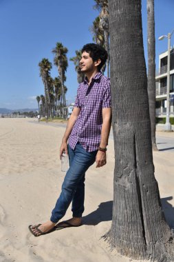Yakışıklı bir genç adam bir palmiye ağacı karşı sahilde yaslanmış