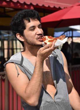 Yakışıklı bir çok etnik gruptan oluşan genç adam açık havada bir dilim biberli pizza yeme.