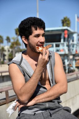 Mutlu bir çok etnik gruptan oluşan genç adam bir cankurtaran kulübe tarafından iskelede bir dilim pizza yeme