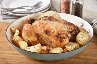 Bir bütün tavuk bebek patates ile bir emaye kaplamalı dökme demir tavada kavrulmuş.