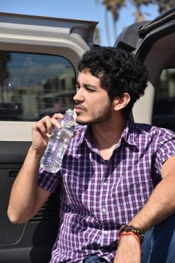 Yakışıklı bir genç adam arabasını Bagaj kapağı üzerinde şişelenmiş su içme tutum ile.